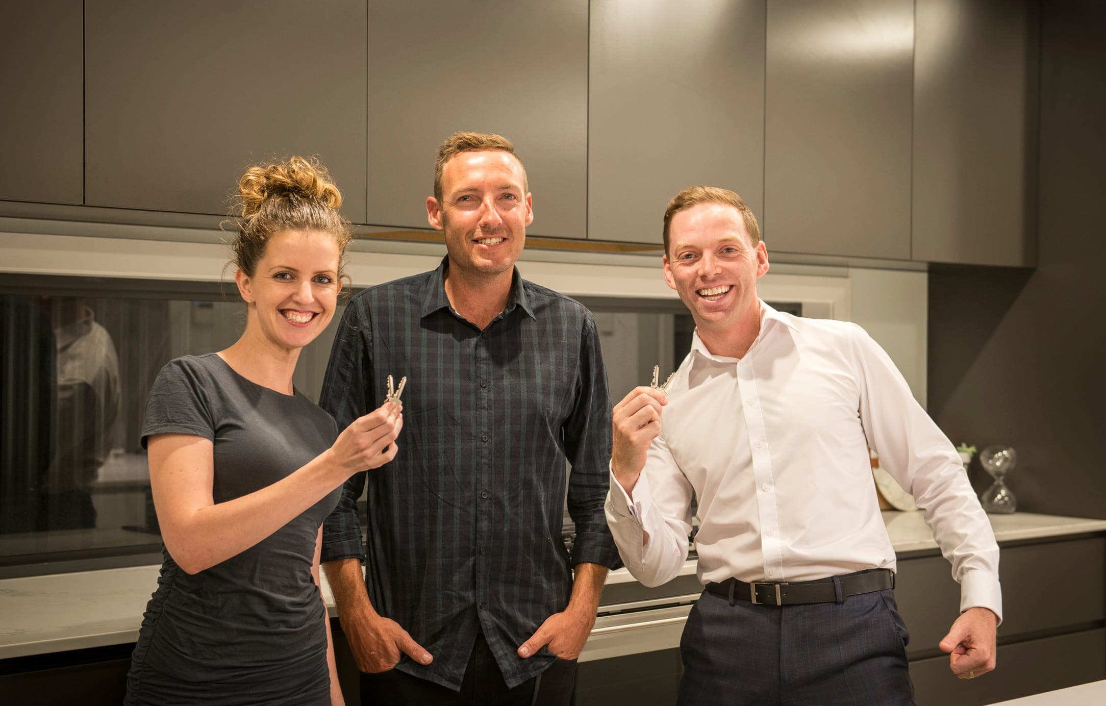 Justin with clients holding the keys to their new home, standing in its finished kitchen