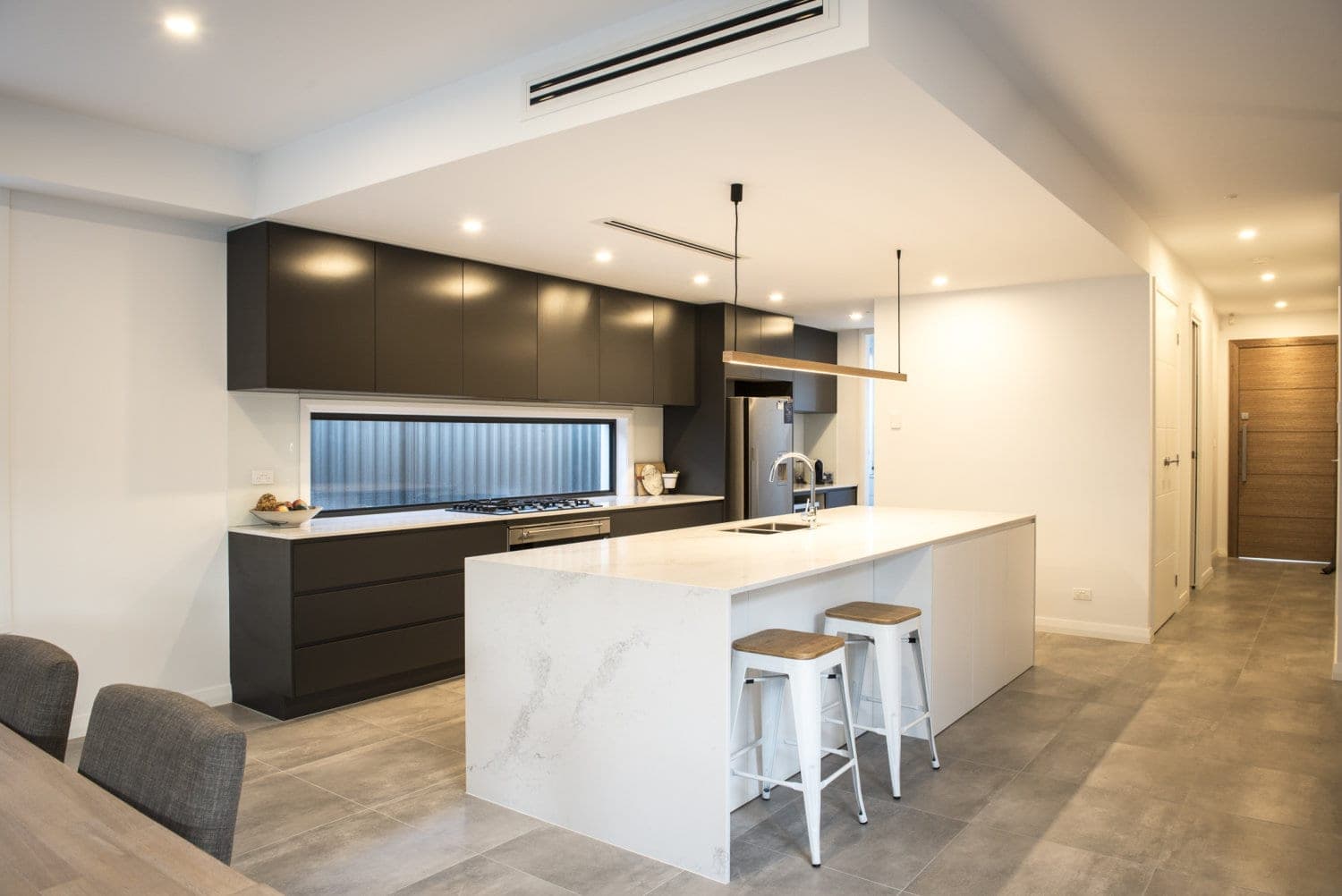 Open-plan kitchen with a marble waterfall island, charcoal cabinetry and a timber pendant light