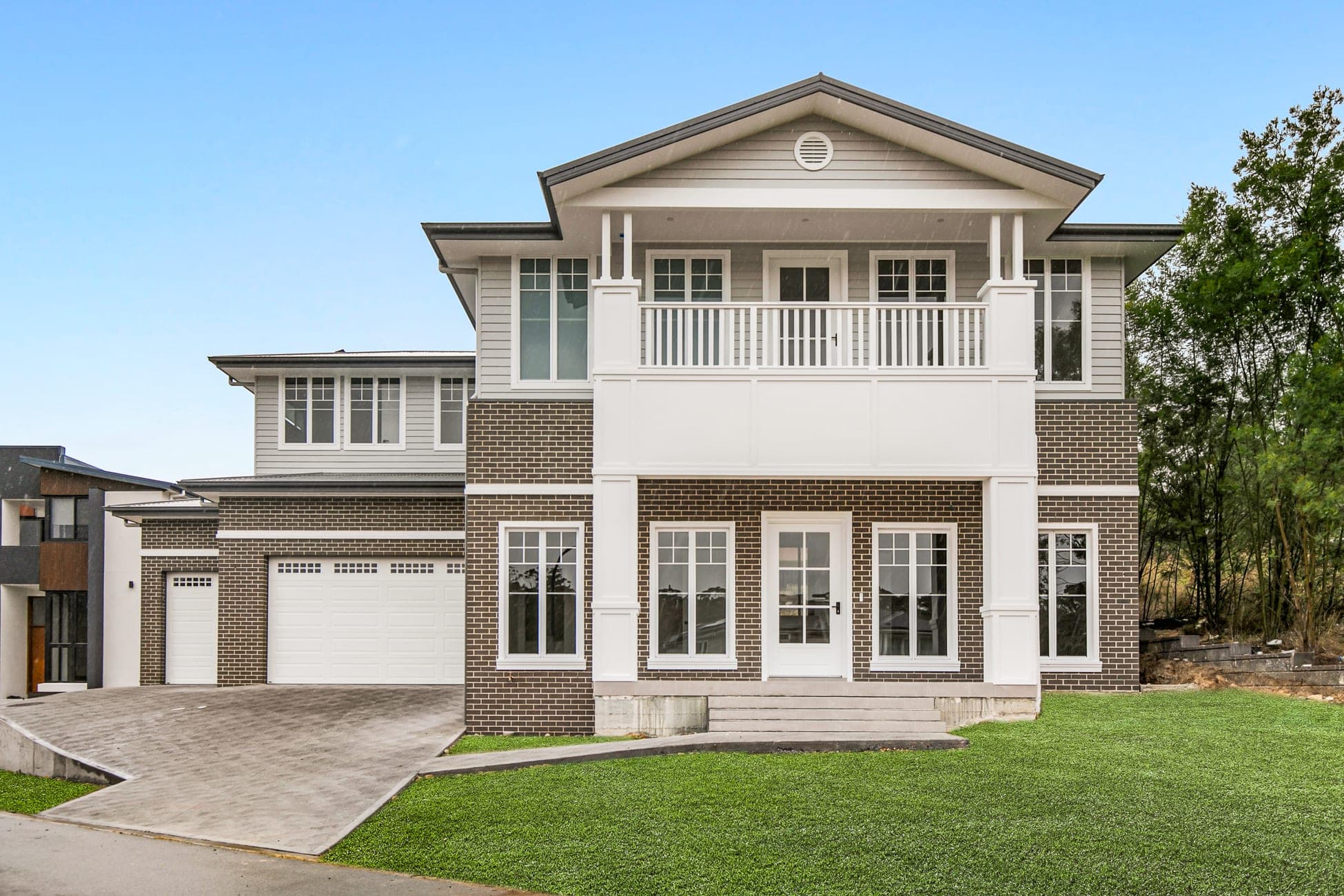 Two-storey Hamptons-style home with white balustrade balcony and brick base